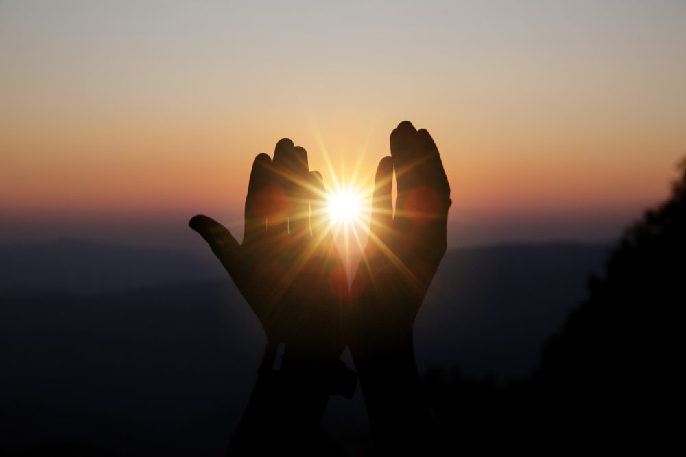 Manos en gesto de recogimiento sosteniendo la luz del atardecer, símbolo de espiritualidad, memoria y trascendencia en una despedida consciente