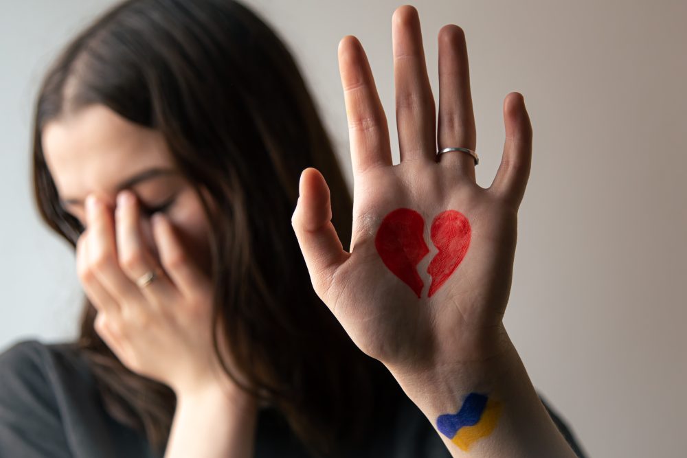 Mujer en duelo cubriéndose el rostro mientras levanta la mano con un corazón roto dibujado, simbolizando dolor emocional y pérdida