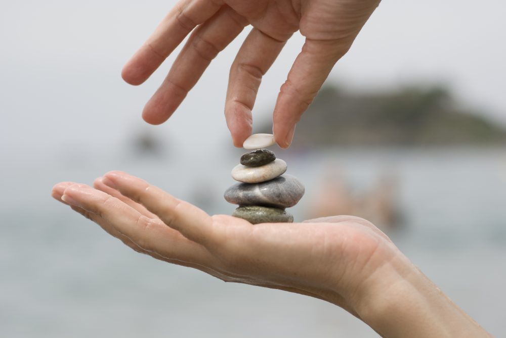 Manos equilibrando piedras sobre otra mano como símbolo de memoria, equilibrio y reflexión sobre la vida y la muerte