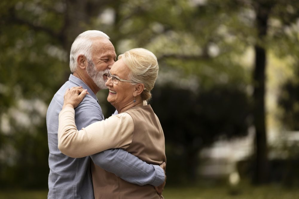 Pareja de adultos mayores abrazándose con cariño en un parque, símbolo del vínculo que permanece en el duelo de la tercera edad