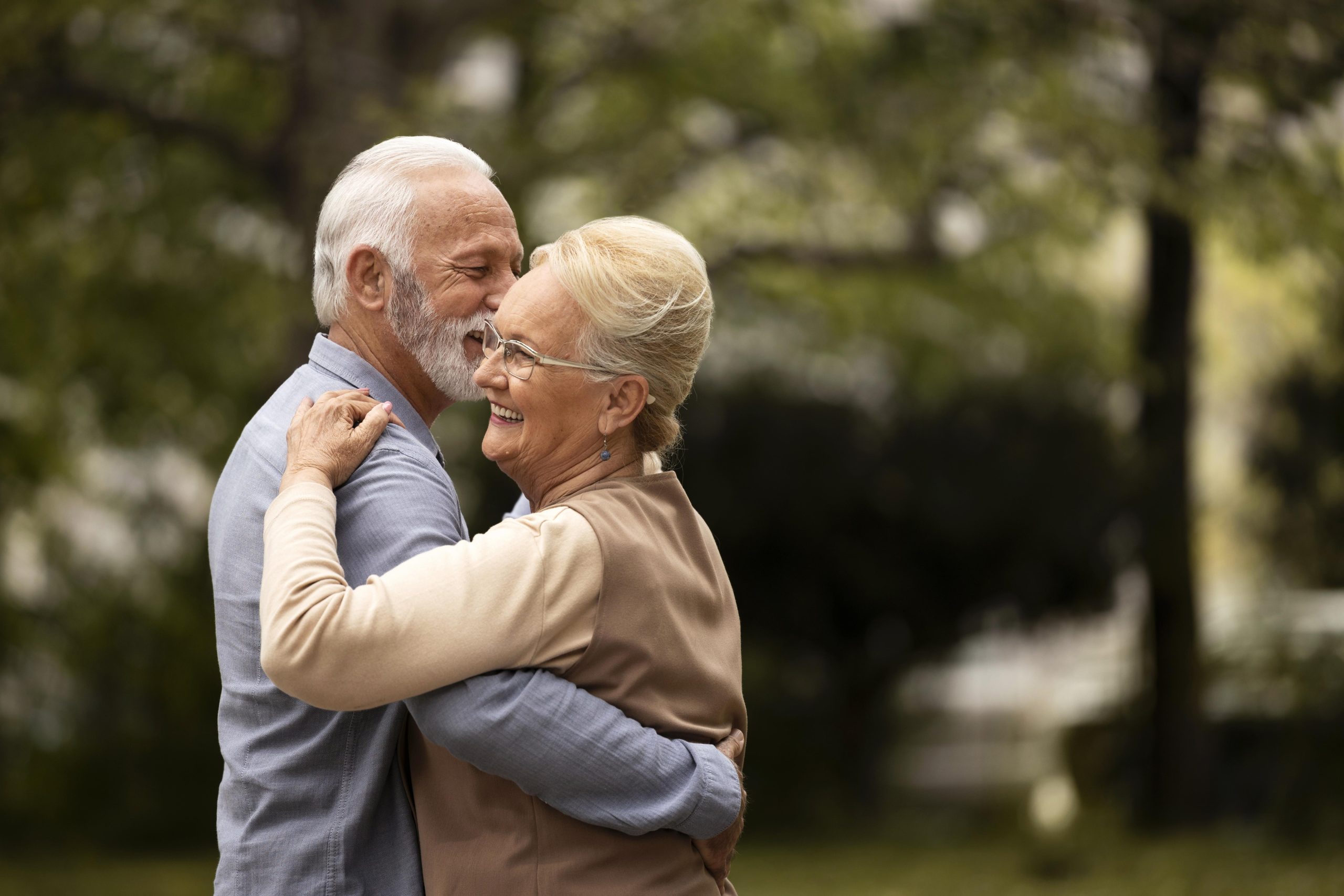 Pareja de adultos mayores abrazándose con cariño en un parque, símbolo del vínculo que permanece en el duelo de la tercera edad